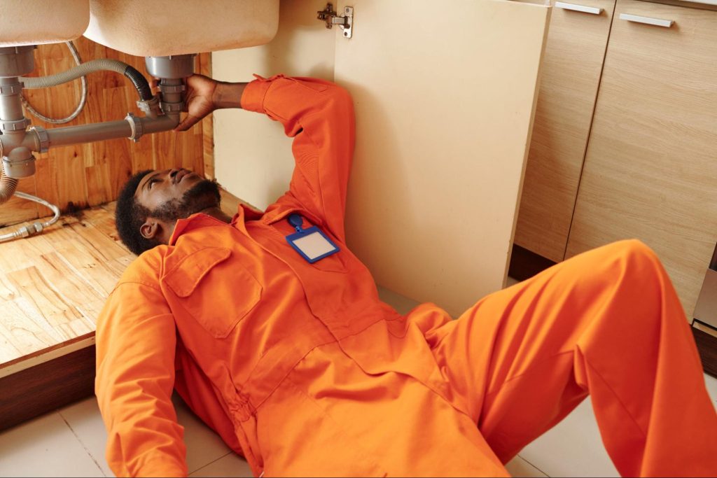 Plumber working on plumbing under a sink.