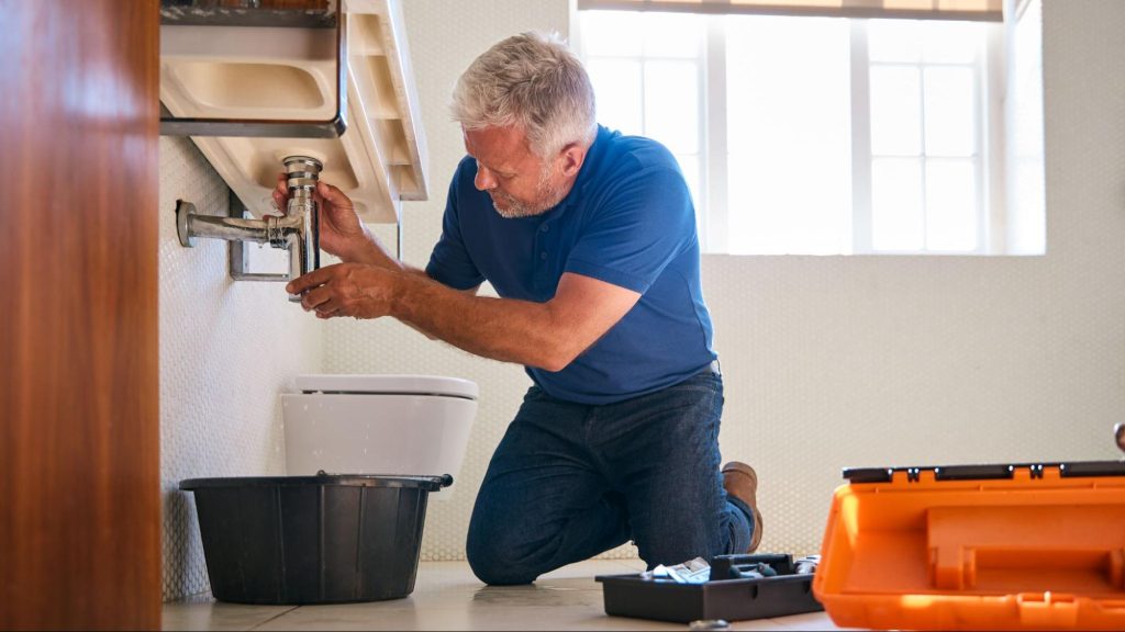 Male plumber checking a leak under a sink.