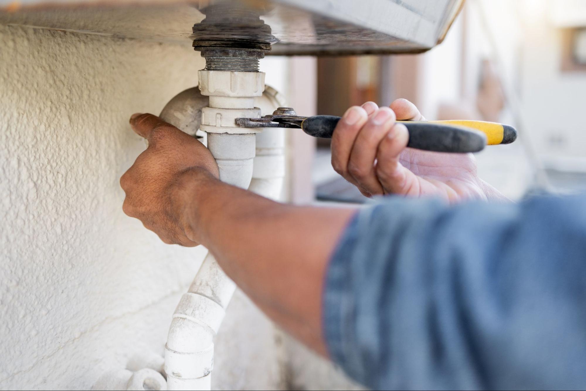 Plumber using a wrench for pipe maintenance and clearing a blockage.