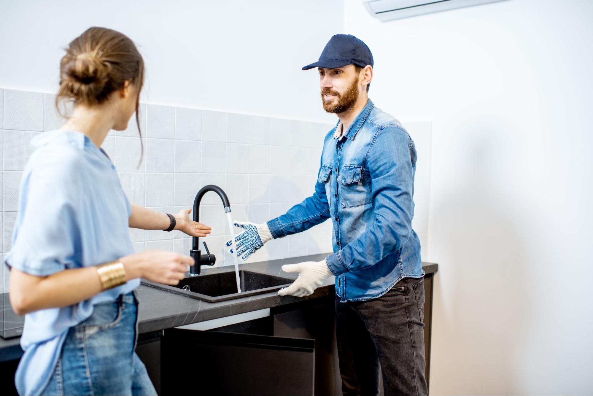 A plumber demonstrating kitchen faucet water flow to a homeowner after repair.
