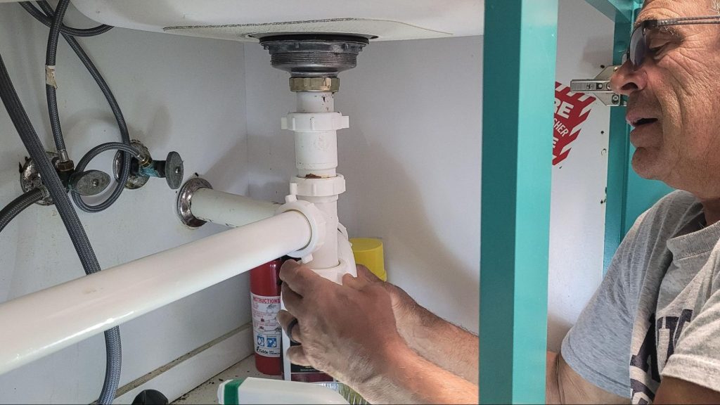 A professional plumber under the kitchen sink repairs utilities to stop a water leak.