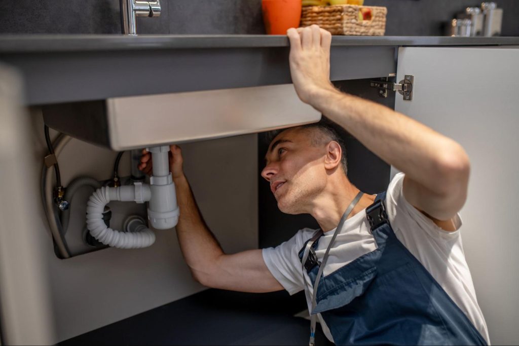 A plumber carefully inspects the underside of a sink and its pipe.