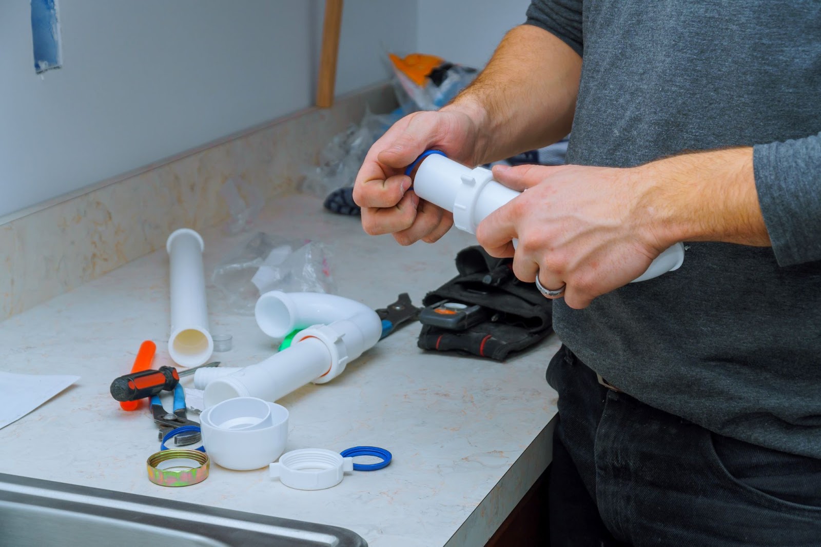 A plumber assembling and installing a kitchen sink with pipes, tools, and fittings