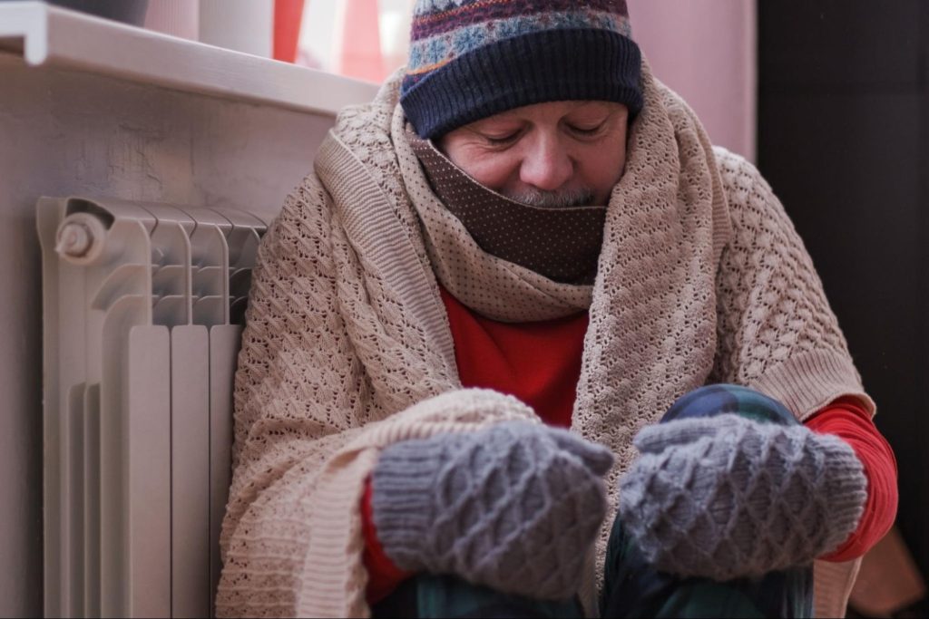 Frustrated man feeling cold indoors while waiting for emergency heating services.