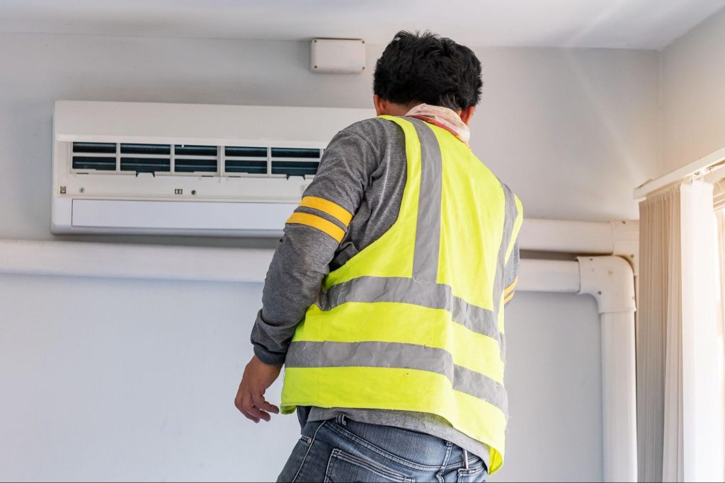 Rear view of an HVAC technician performing indoor maintenance on a wall-mounted air conditioning unit.