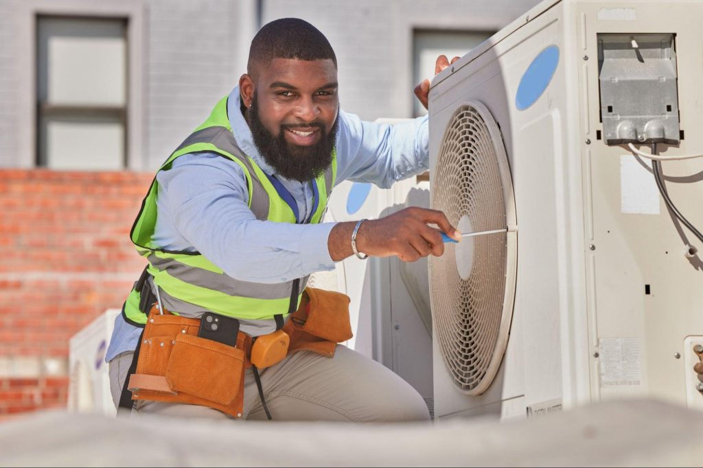 A smiling technician performs AC repair and maintenance on an outdoor unit.