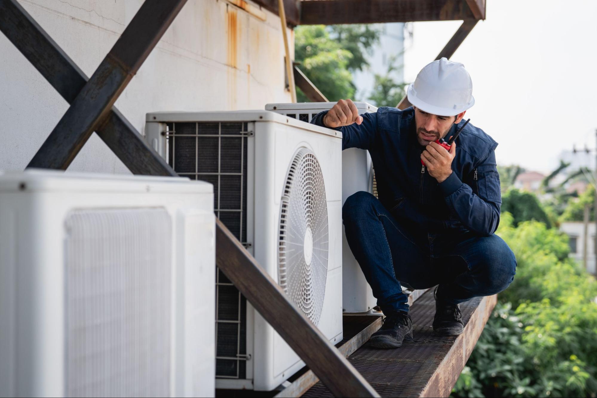 An HVAC technician inspects the cooling system of a building, reporting issues via two-way radio