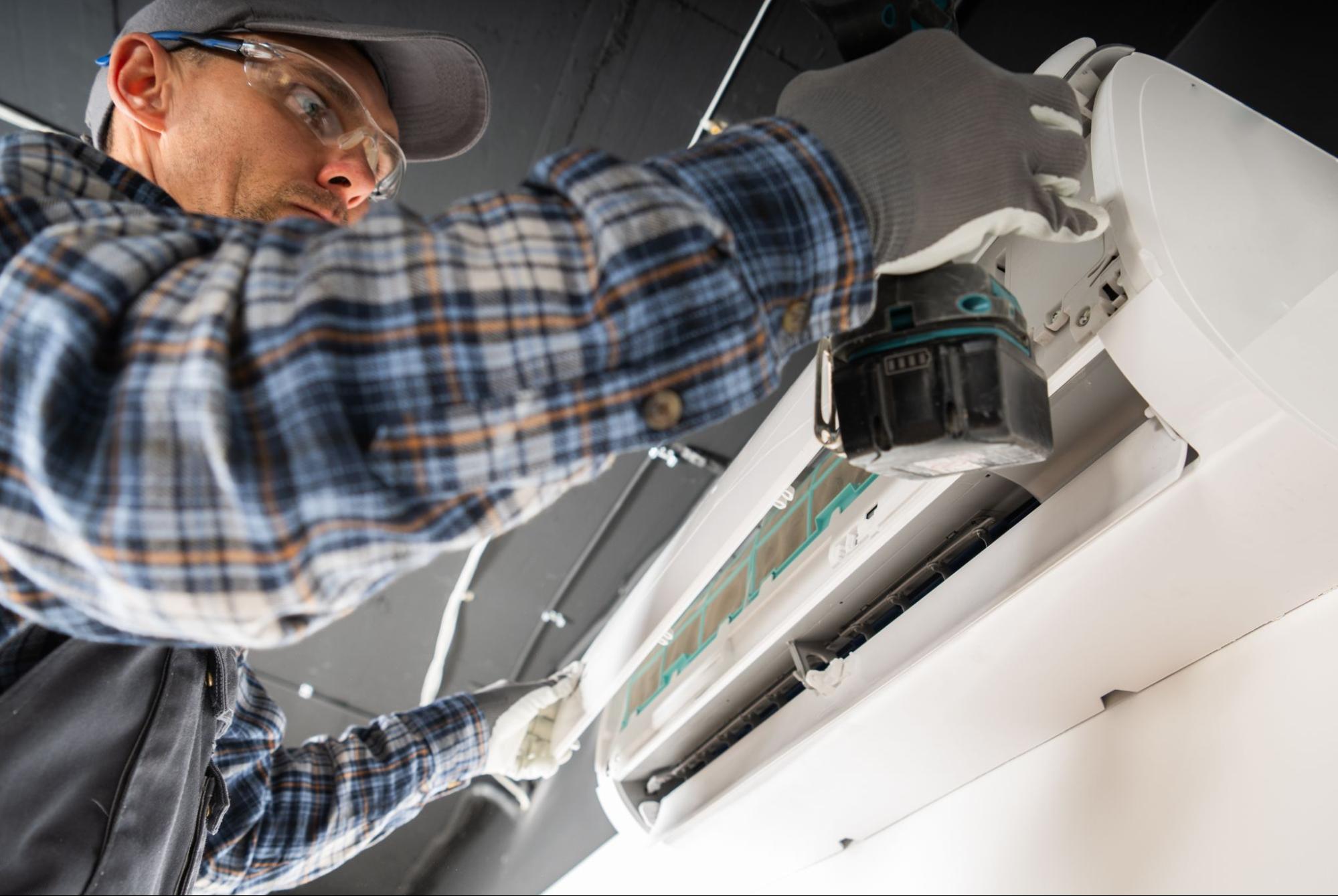 A close-up of a technician performing maintenance on a split-type air conditioning unit.