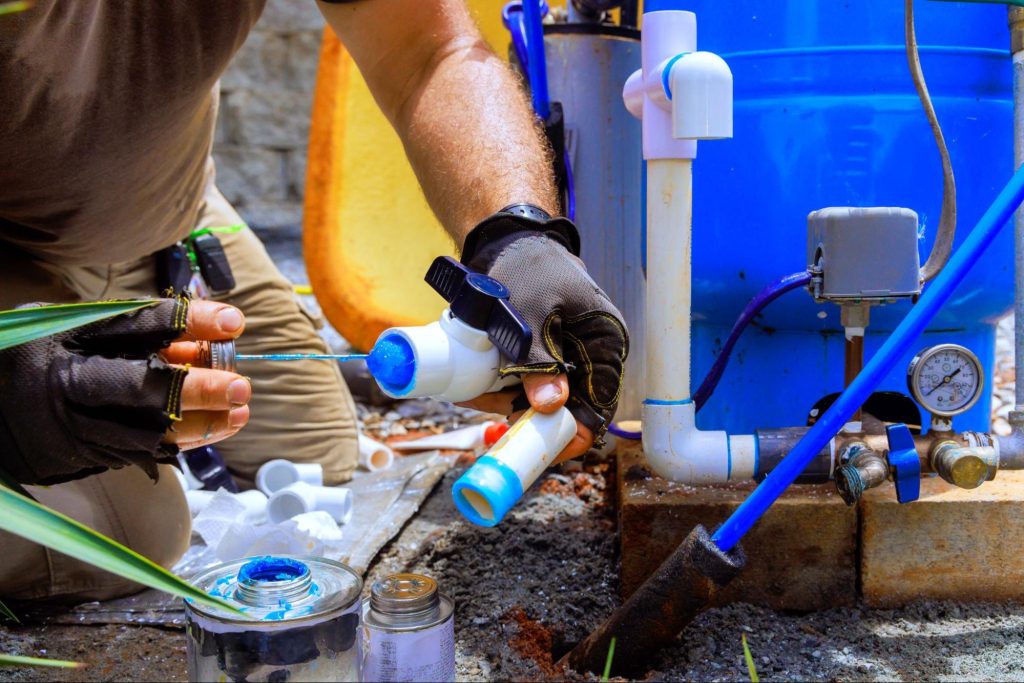 A plumber is gluing PVC pipes in a pump house connected to a water softener system for an artesian well.