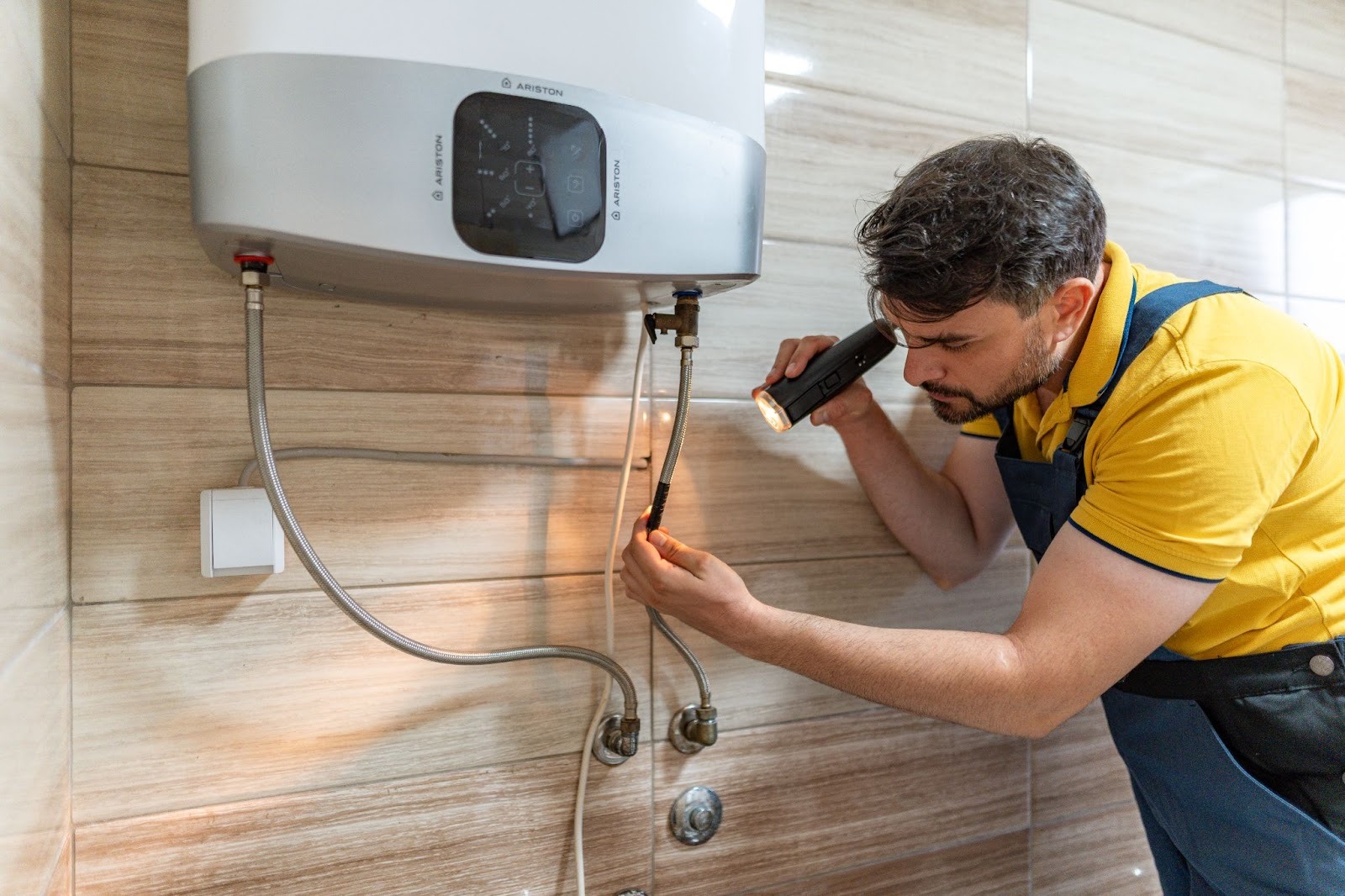 A skilled technician uses a flashlight to inspect and repair a water heater in a clean, modern bathroom