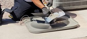 An HVAC technician carefully cleans the condenser fan blades of a residential air conditioning unit during routine service