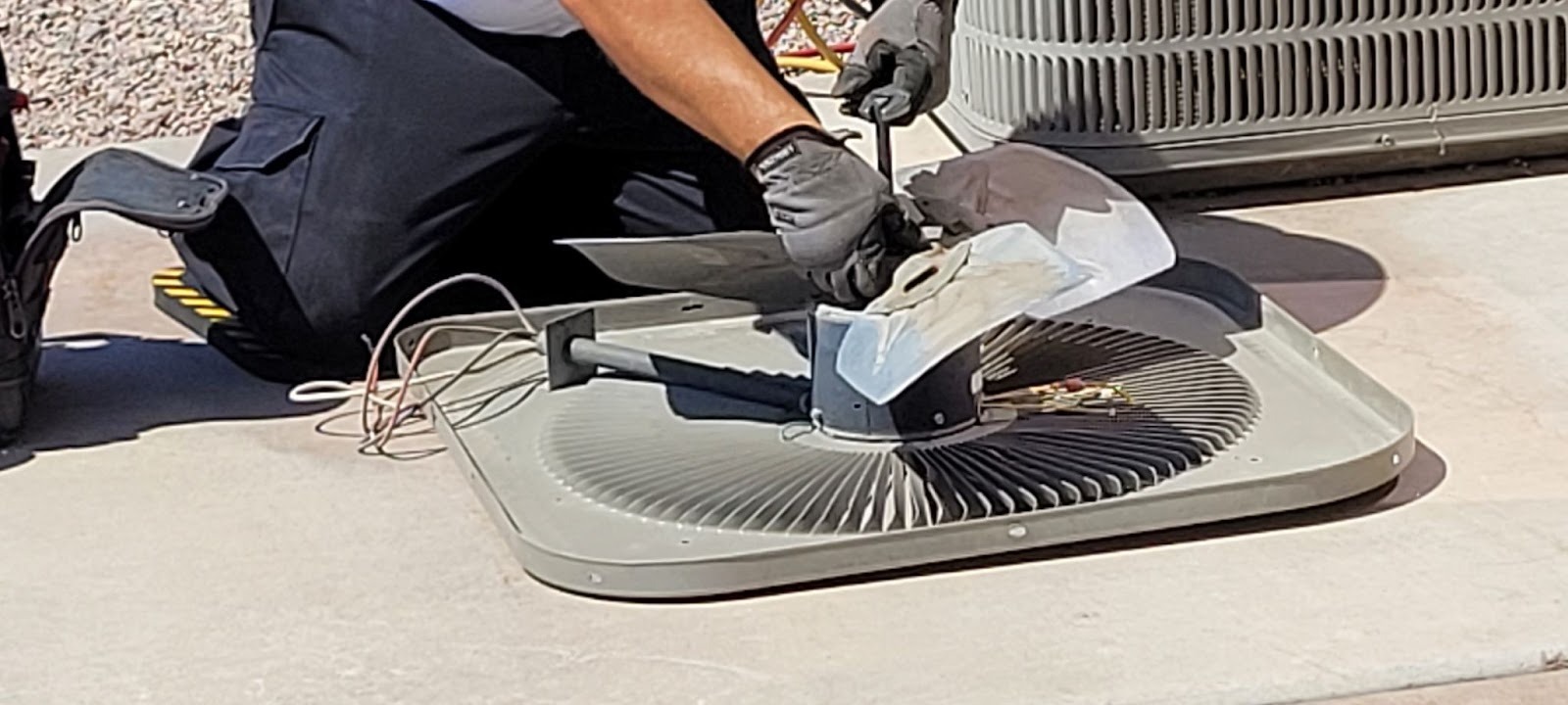 An HVAC technician carefully cleans the condenser fan blades of a residential air conditioning unit during routine service