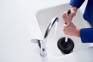 Overhead view of a plumber using a plunger to clear a clogged household drain