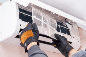 A close-up of a person’s gloved hands repairing an indoor air conditioning system.