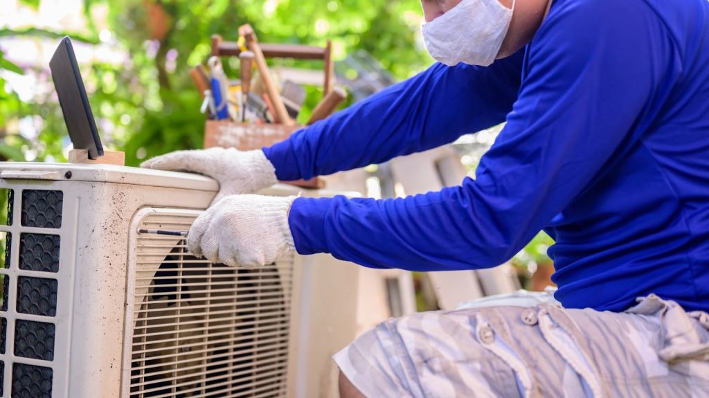 A man wearing gloves is unscrewing the side of an air conditioning unit to repair it.