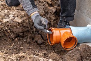 A plumber pointing at a plastic pvc waste sewer pipe on the ground.