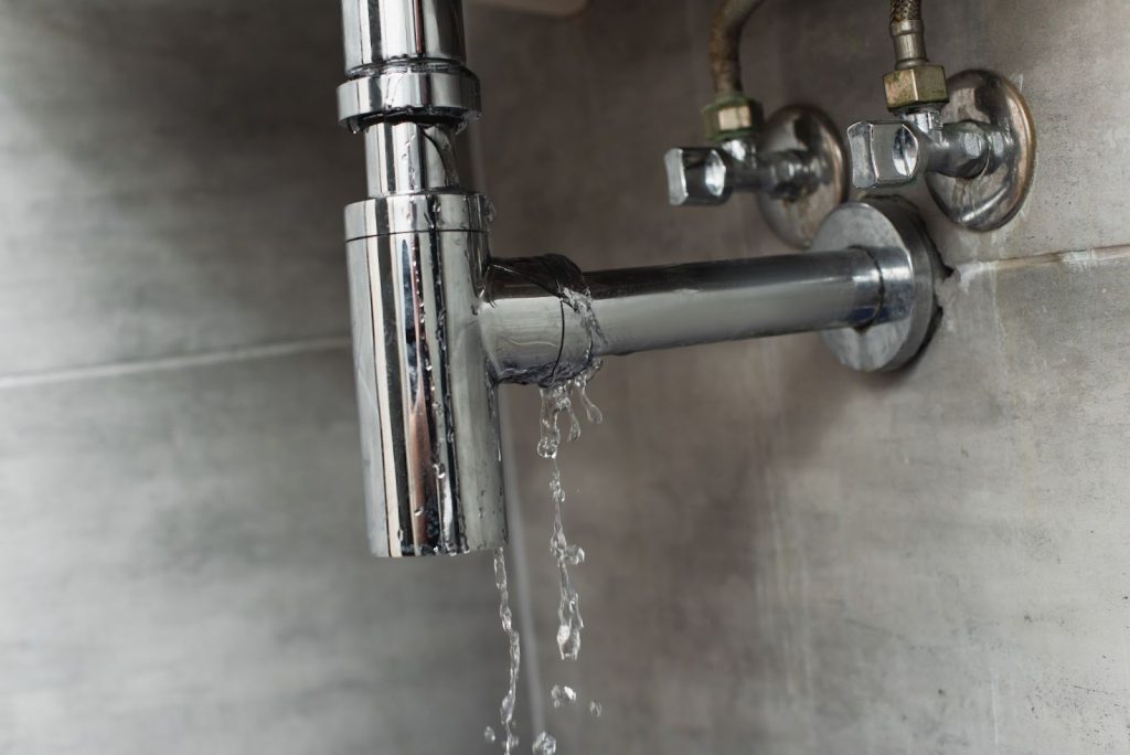 Cracked sink pipe with active leak on a gray surface