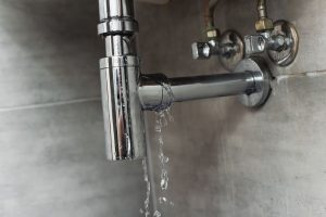 Cracked sink pipe with active leak on a gray surface