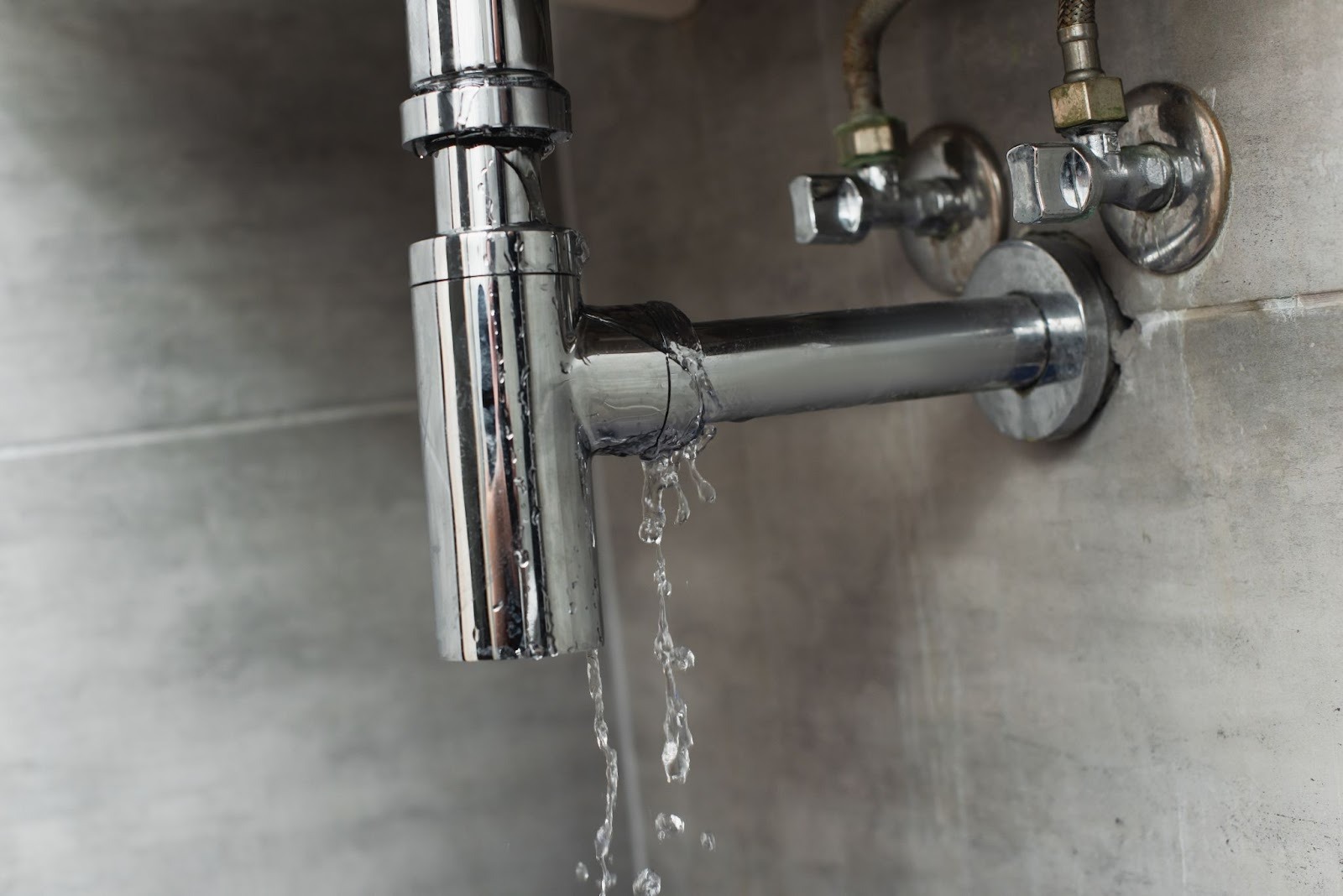 Cracked sink pipe with active leak on a gray surface
