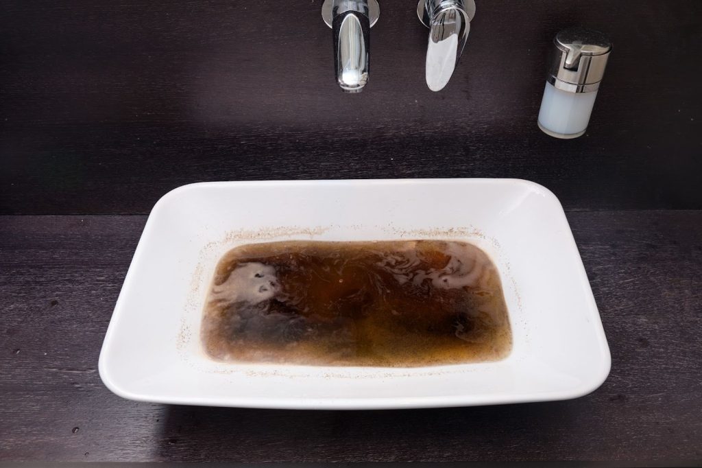 Blocked modern white bathroom sink with standing water and visible drain obstruction