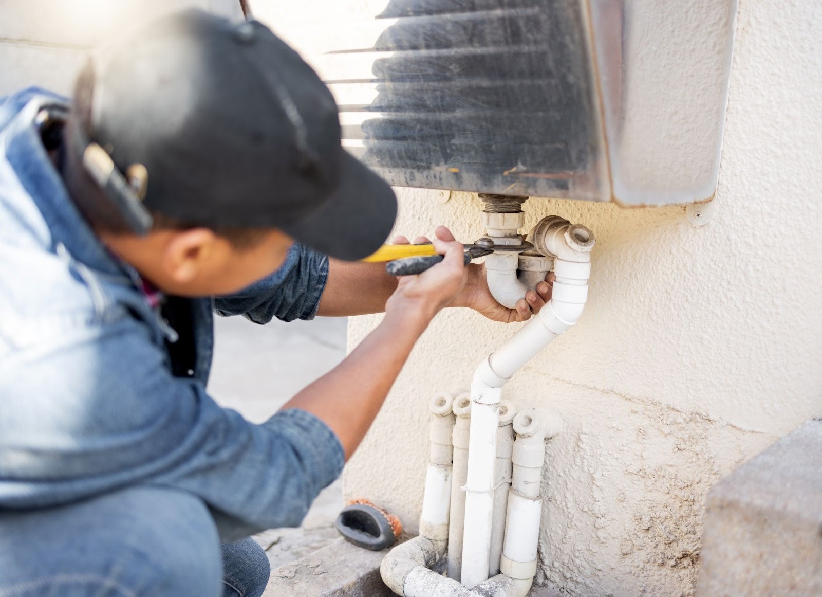 A plumber working on water pipe repairs with a wrench inside a building maintenance area