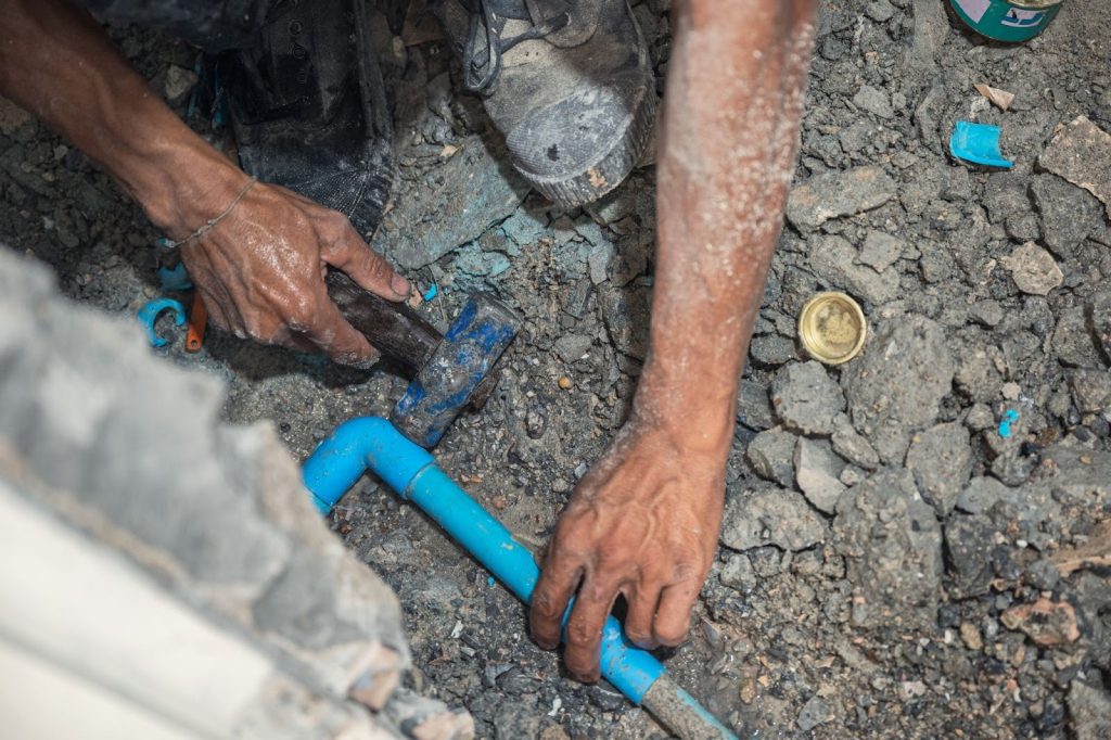 A plumber hammering a PVC pipe during a bathroom plumbing repair