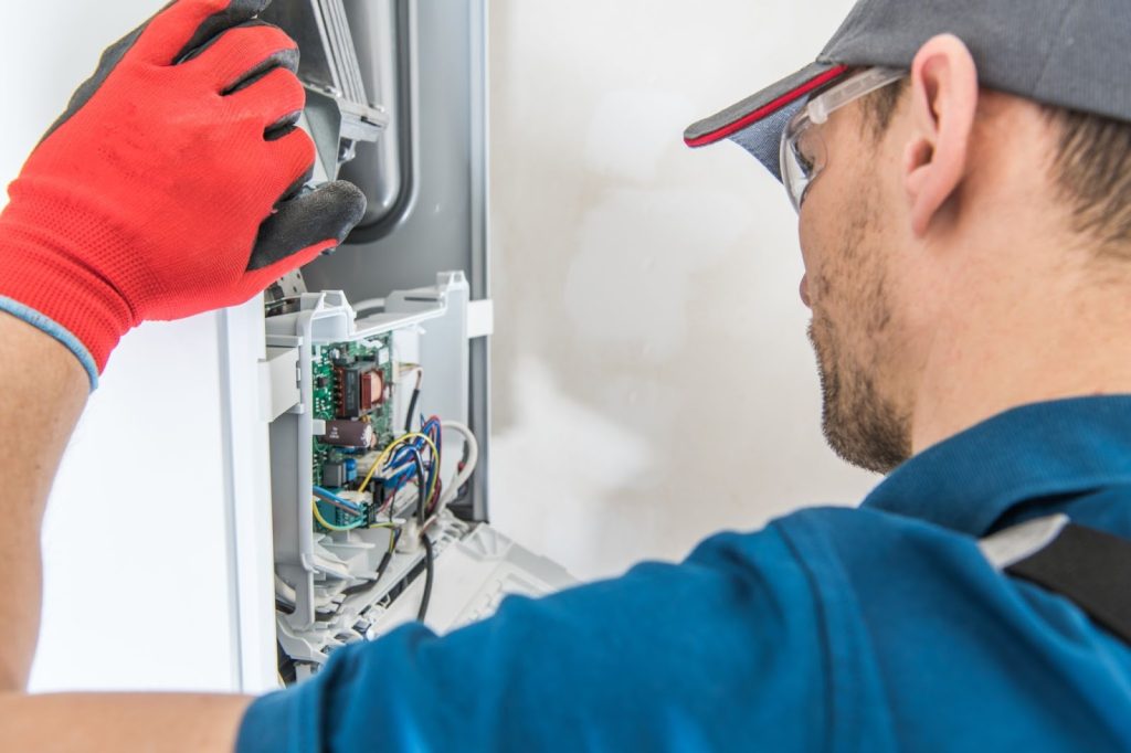 Side view of a technician inspecting a gas furnace during a repair service