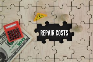 Wooden puzzle spelling “repair costs” beside a red calculator, paper money, and a small caution sign