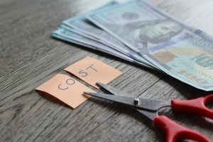 Scissors slicing a “COST” note into two pieces beside the dollar bills on the right