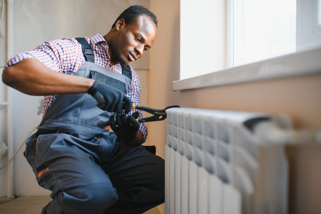 Technician in workwear overalls repairs a heating radiator indoors using hand tools