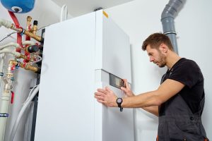 HVAC technician installing a furnace system in a basement, connecting gas pipes, and attaching an expansion tank