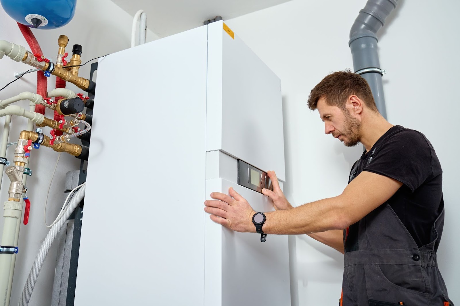 HVAC technician installing a furnace system in a basement, connecting gas pipes, and attaching an expansion tank